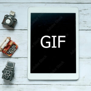 Top view of toys camera,typewriter and tablet written with GIF on white wooden background.