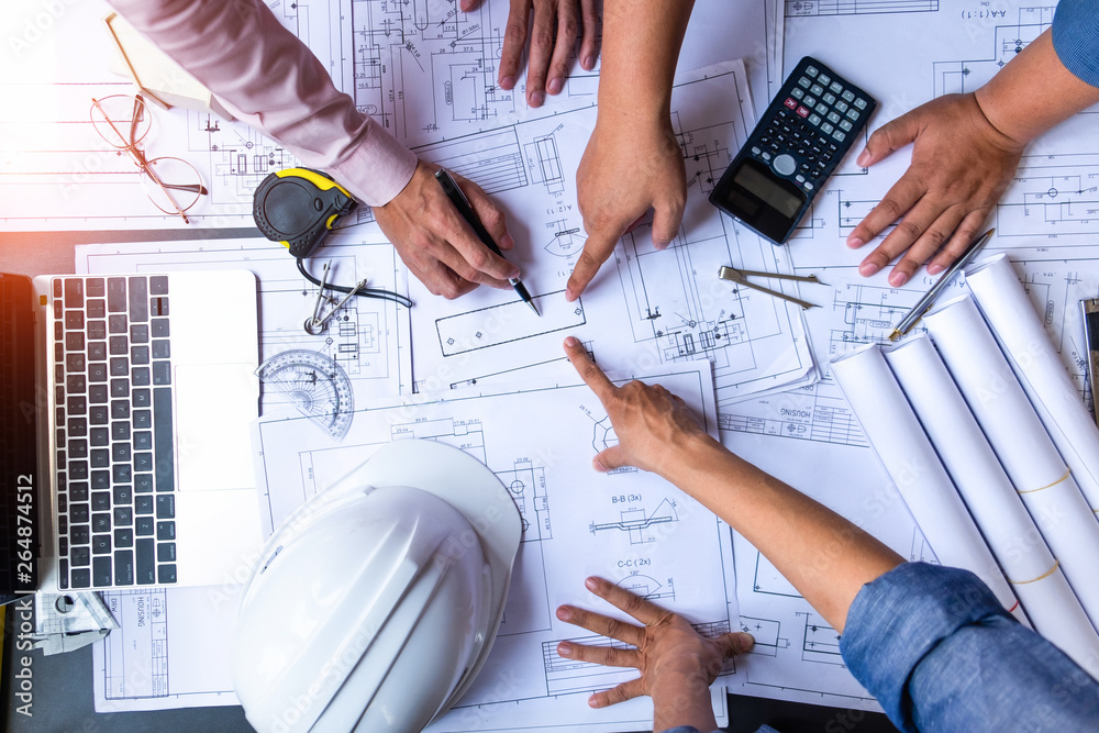 engineers pointing to building on blueprint and using laptop to drawing design building Project in office, construction concept. Engineer concept