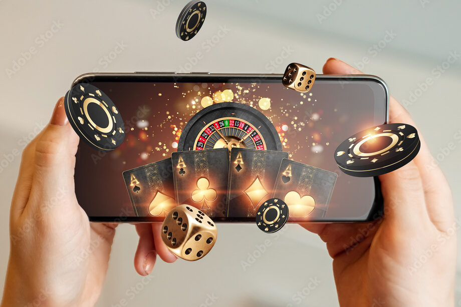 Creative background, online casino, in a man's hand a smartphone with playing cards, roulette and chips, black-gold background. Internet gambling concept. Copy space