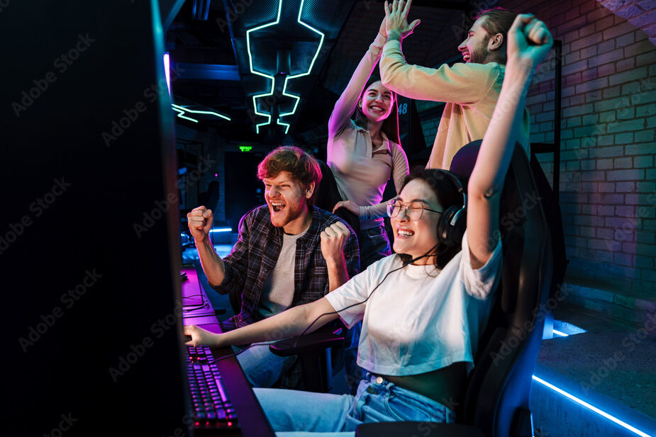 Group of friends celebrating victory of asian girl in video game while standing next to her in cybersport club