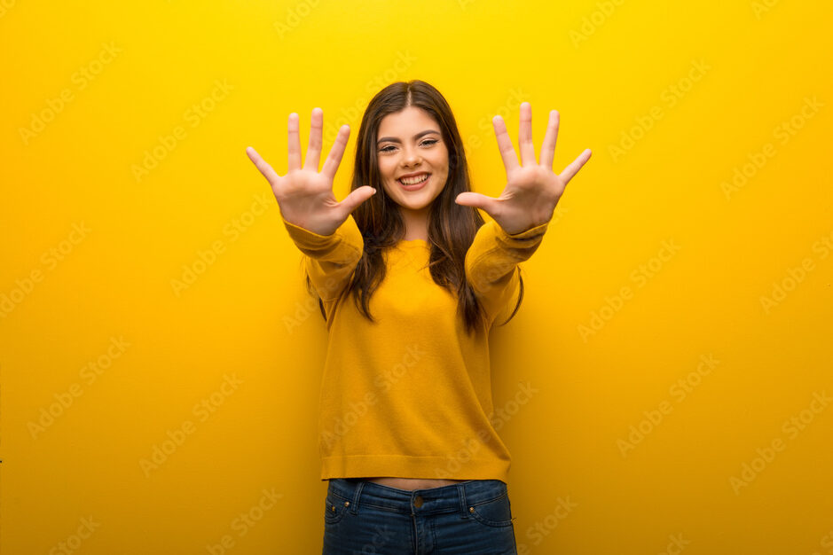 Teenager girl on vibrant yellow background counting ten with fingers